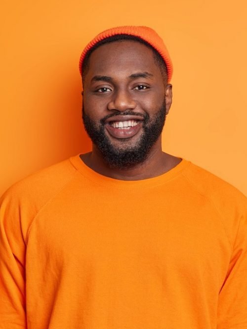 waist-up-shot-of-happy-black-man-smiles-happily-dressed-in-orange-hat-and-sweater-being-in-good-mood-e1627313512303.jpg